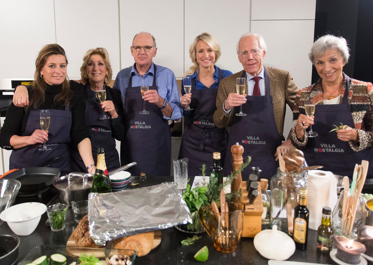Zes journaalpresentatoren in keukenschorten met een glas in de hand in de studio van Villa Nostalgia