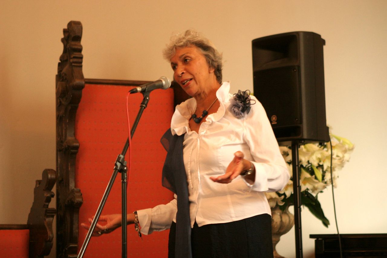 Eugènie speaking into a microphone on a stage during a cultural programme